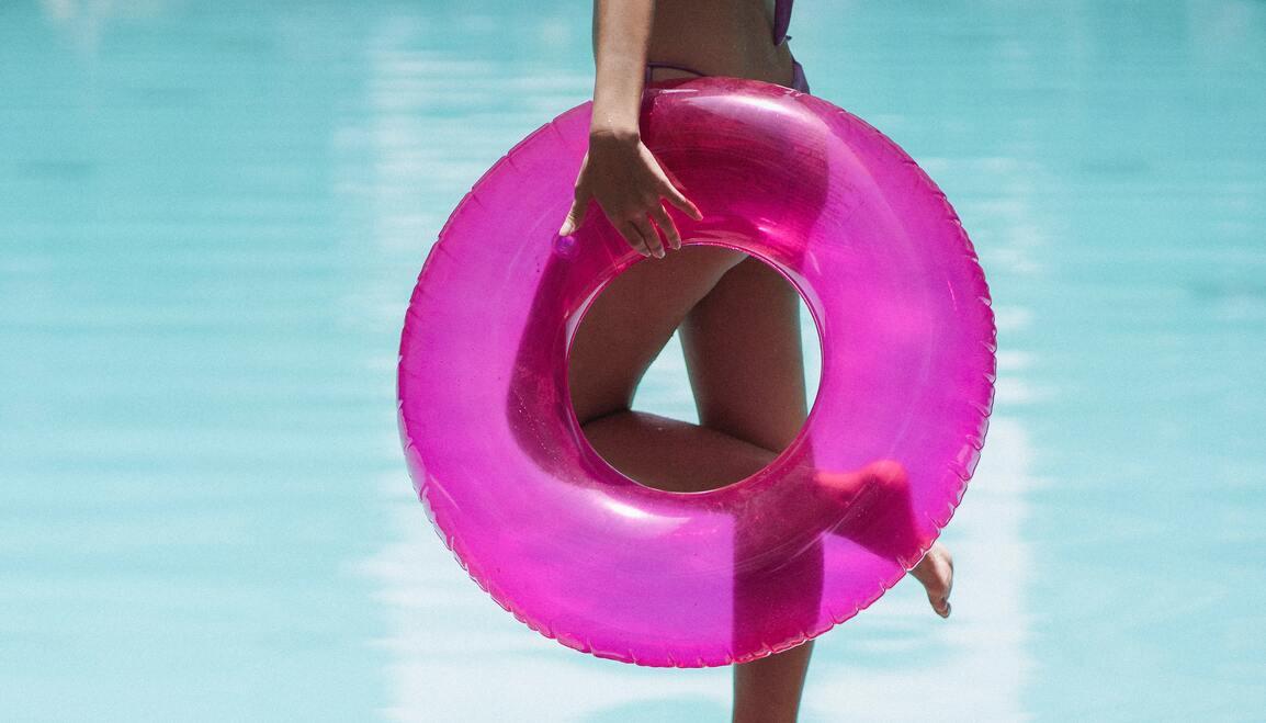 Jeune femme à l'aise dans son corps qui rentre dans son maillot à la veille de l'été grâce à l'hypnose, bouée rose fluorescente à la main